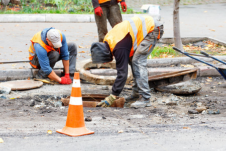 一队修路工人正在用一个新的更换旧的下水道检修孔。