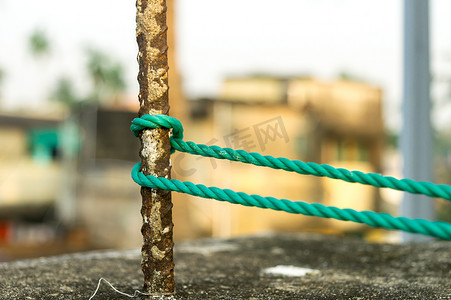 一根绳子在栅栏柱周围打结，绳子在一根与背景隔离的生锈铁杆上打结。