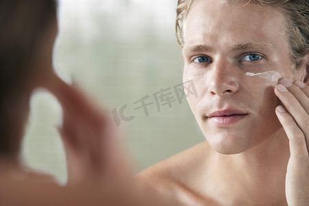 清爽浴室摄影照片_一个年轻人在脸上涂面霜的镜面反射