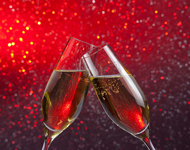 紫色气泡饮料摄影照片_红色和紫色光散景背景上带有金色气泡的香槟长笛