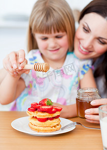 可爱蜂蜜摄影照片_可爱的小女孩和她妈妈把蜂蜜放在华夫饼上