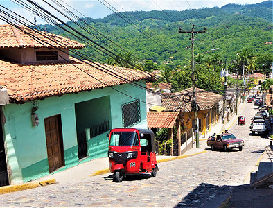 红色城市车摄影照片_洪都拉斯、科潘、有红色嘟嘟车和汽车的街道