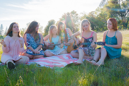 草地音乐摄影照片_女孩们坐在一起在草地上唱歌和演奏音乐