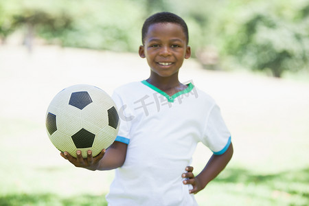 在公园里拿着足球的小男孩对着镜头微笑