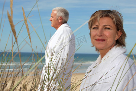 一对成熟的夫妇在海滩上穿着浴袍。