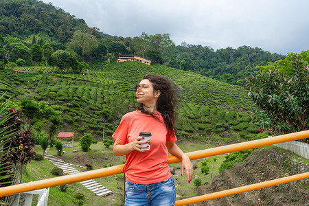 在绿茶谷的背景下，黑发旅游女孩享用工艺杯中的茶。
