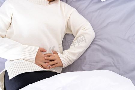 肚腹摄影照片_躺在床上肚子疼的年轻女人。