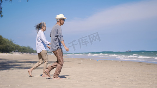 高级男女夫妇手牵着手走到阳光明媚的海滩，蓝天明媚