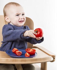 小孩餐具摄影照片_小孩在高脚椅上吃西红柿