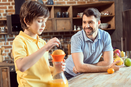 微笑的父亲看着小儿子在厨房里榨新鲜果汁