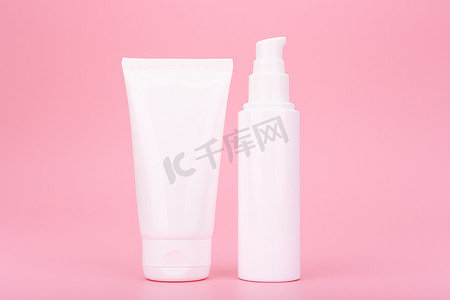 两个白色化妆品瓶，上面有奶油、乳液或磨砂膏，用于粉红色背景的面部或手部