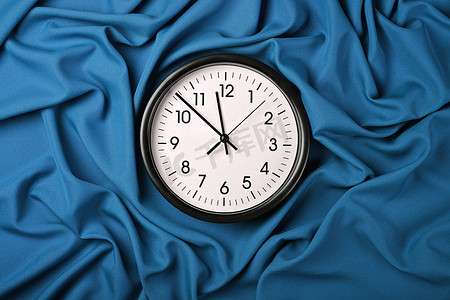 扭曲的时钟摄影照片_蓝色织物折叠褶上的白色时钟