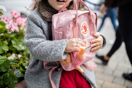 身后有花的小女孩抱着粉色背包和小洋娃娃