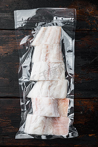 鳕鱼包装摄影照片_黑线鳕鱼在真空包装中去皮，深色木质背景，顶视图