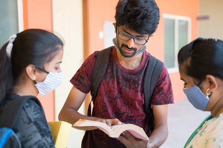一群戴着医用口罩的大学生在大学校园走廊里翻阅书籍进行讨论 — 大学重新开放、团结和友谊的概念。