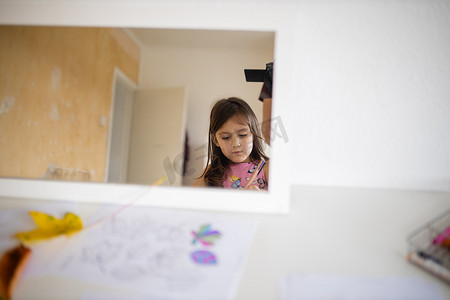 白桌上的镜子反射着一个小女孩和一扇白色敞开的门