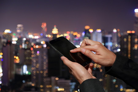 女人手触摸屏智能手机，手机上模糊抽象散景夜城市背景作为社会概念。