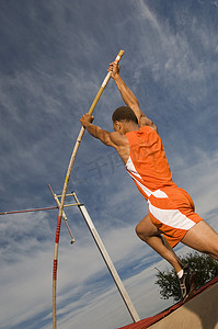 一条腿站立摄影照片_一名男运动员在天空中进行撑杆跳高的低视角