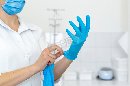 戴手套的护士摄影照片_在明亮的处理室里，一名身穿白大褂的护士在进行医疗程序前戴上橡胶手套。