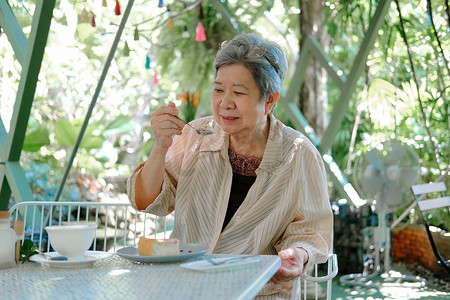 在餐厅吃芝士蛋糕的亚洲老妇人