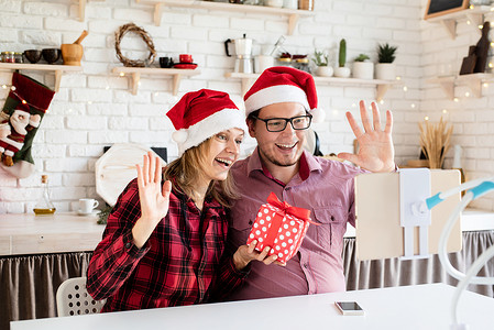 戴着圣诞帽的快乐年轻夫妇在平板电脑上的视频通话中问候他们的朋友