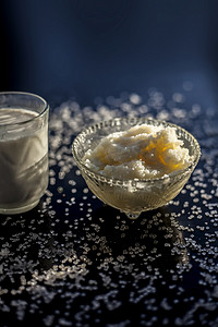 关闭玻璃碗纯牛奶与热牛奶在黑色木质光滑表面上充分混合，以及生酥油澄清黄油和一些糖晶体散布在表面上。