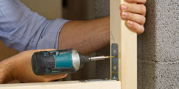 Craftman 拿着一把便携式螺丝刀，用于将金属角固定在木板上。