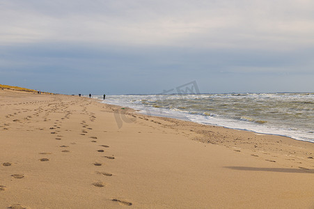 强风吹拂摄影照片_人们在强风中在沙滩上散步