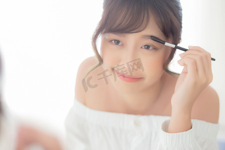 女性眉毛摄影照片_美丽的年轻亚洲女人化妆眉毛刷，男朋友