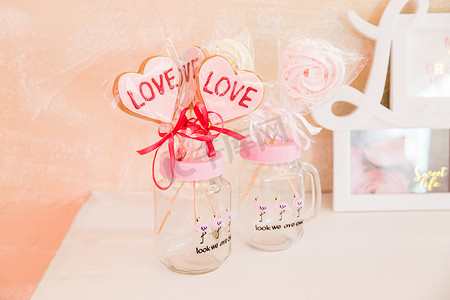 可爱粉色装饰摄影照片_情人节装饰透明玻璃罐中的棍子上的糖果