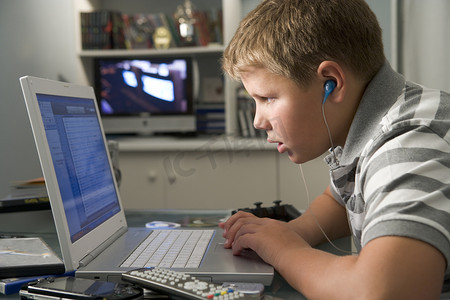 看电视的小男孩摄影照片_小男孩在卧室里用笔记本电脑听 MP3 播放器