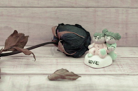 陶瓷娃娃摄影照片_木纹背景颜色的干玫瑰和陶瓷娃娃