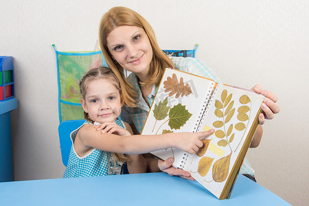 五岁的女孩和母亲正在检查相册中一张纸上的植物标本室展示，然后看着相框