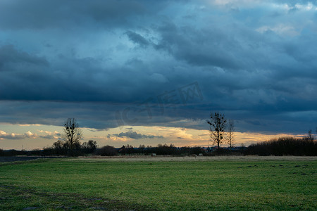 草地下雨摄影照片_绿色草地、地平线上的树木和黑暗的暴风云