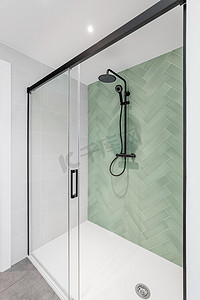 现代浴室配有浅绿色和白色瓷砖、雨淋头、手持淋浴和玻璃门。