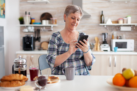 早餐时放松的老妇人在手机上浏览