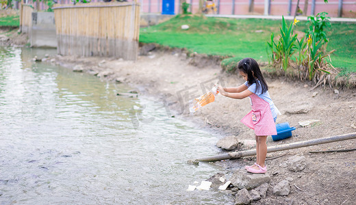 一个小女孩在公园的池塘里喂鱼