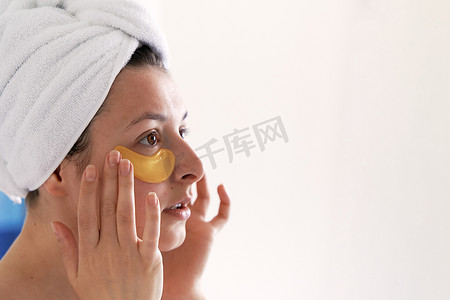 淋浴后，女孩裹着毛巾，并在眼睛下方贴上化妆品贴片。