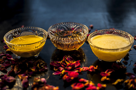 去黑头面膜膏摄影照片_玻璃碗中黑色光滑表面上的 Ayurvedic 保湿面膜，配有一些酥油或澄清黄油、蜂蜜和包装。