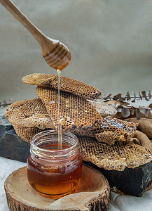 美味的蜂蜜从木制蜂蜜勺滴入玻璃罐和新鲜蜂窝背景中。