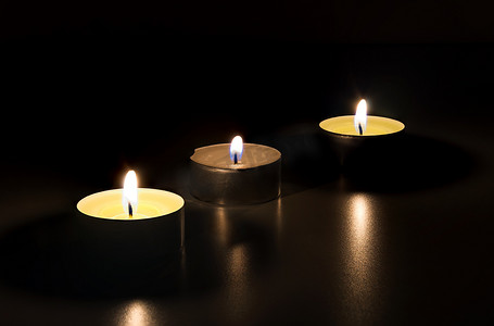 三根蜡烛摄影照片_三根燃烧的蜡烛在黑暗中