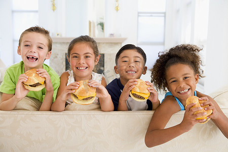 男孩吃汉堡摄影照片_四个小孩在客厅里微笑着吃芝士汉堡