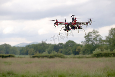 摄像背景摄影照片_六角直升机无人机在乡村背景前盘旋。