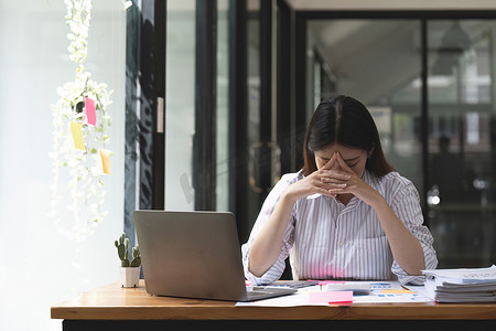 亚洲女性在笔记本电脑上工作时压力很大，疲惫的亚洲女商人在办公室头痛，工作时感觉不舒服