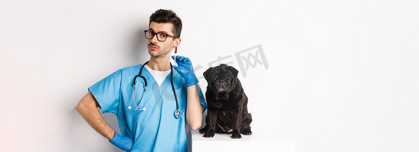 宠物医院背景摄影照片_英俊的兽医医生拿着注射器，站在可爱的黑哈巴狗旁边，为狗接种疫苗，白色背景