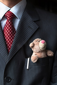 这位优雅时尚的商人将可爱的泰迪熊放在胸前的西装口袋里。