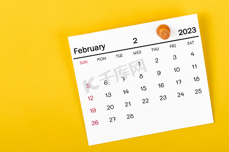 2023 年 2 月的月历和黄色背景的木制图钉。
