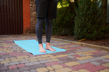 在户外练习瑜伽时，一个活跃的男人、运动员、瑜伽士赤脚站在蓝色健身垫上的剪影