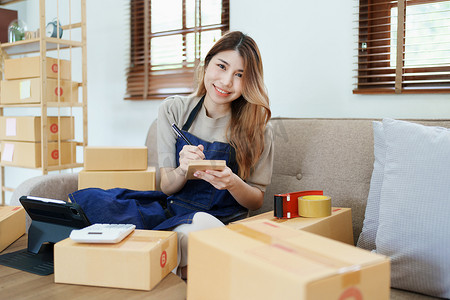独立产品摄影照片_独立的年轻亚洲女性在线卖家的小企业主正在使用计算机并接受订单来包装产品以交付给客户。