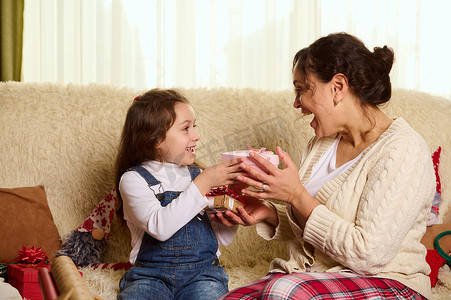 一个慈爱的母亲的幸福家庭和她可爱的女儿在圣诞节假期在舒适的家庭室内交换礼物